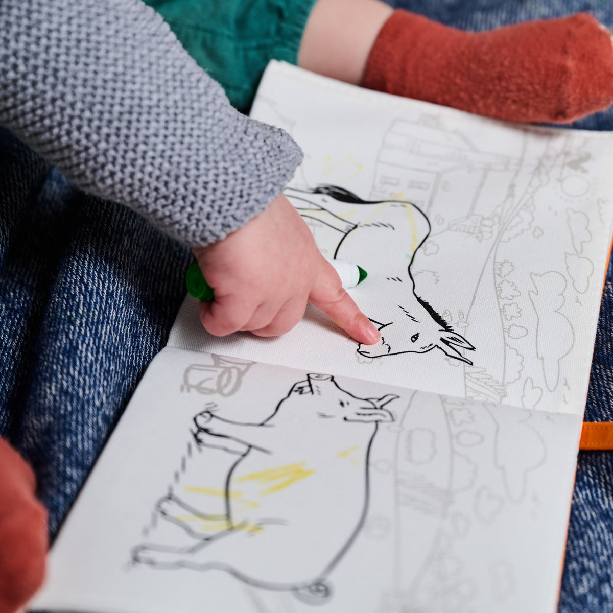 a child's hand points to a page of eatsleepdoodle reusable colouring in book