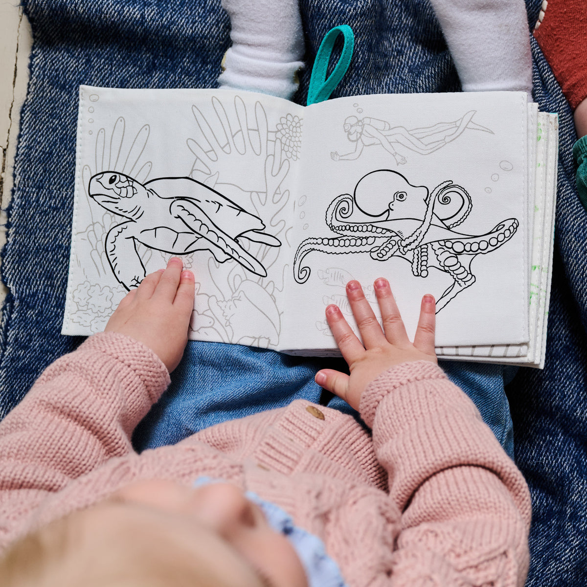 a toddler holds an uncoloured fabric book showing a sea turtles and an octopus
