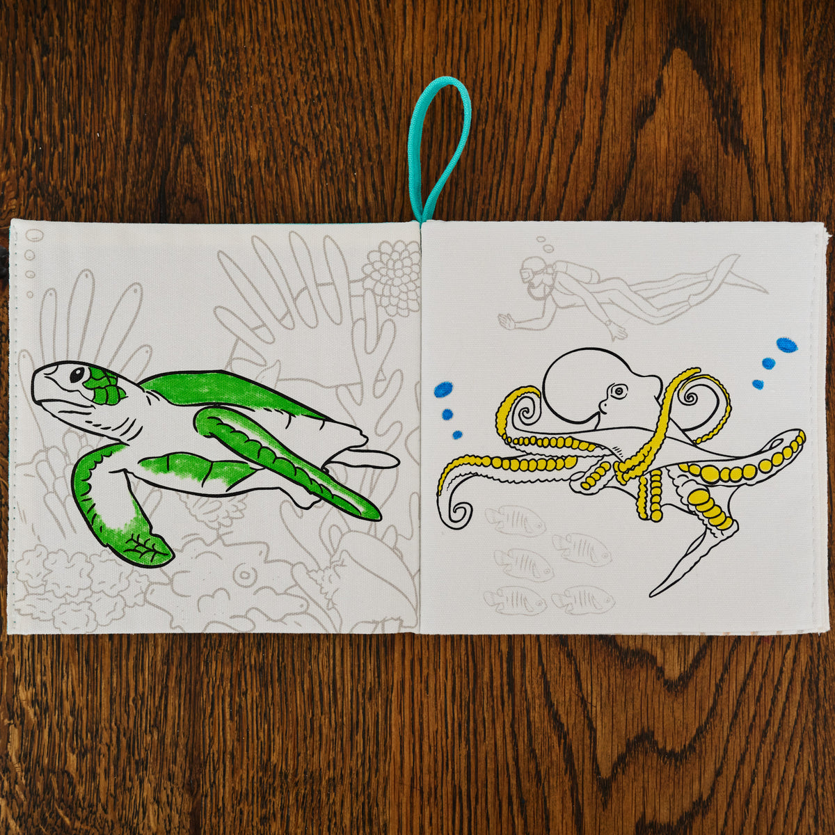 Coloring book open to pages with a green turtle and yellow octopus on a wooden surface.